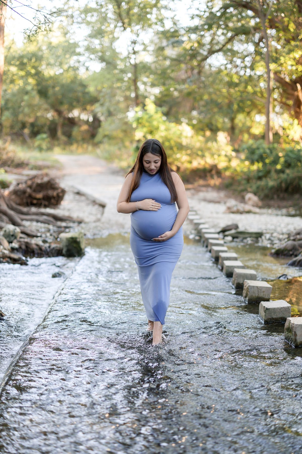 Maternity portrait in a blue dress standing in a creek