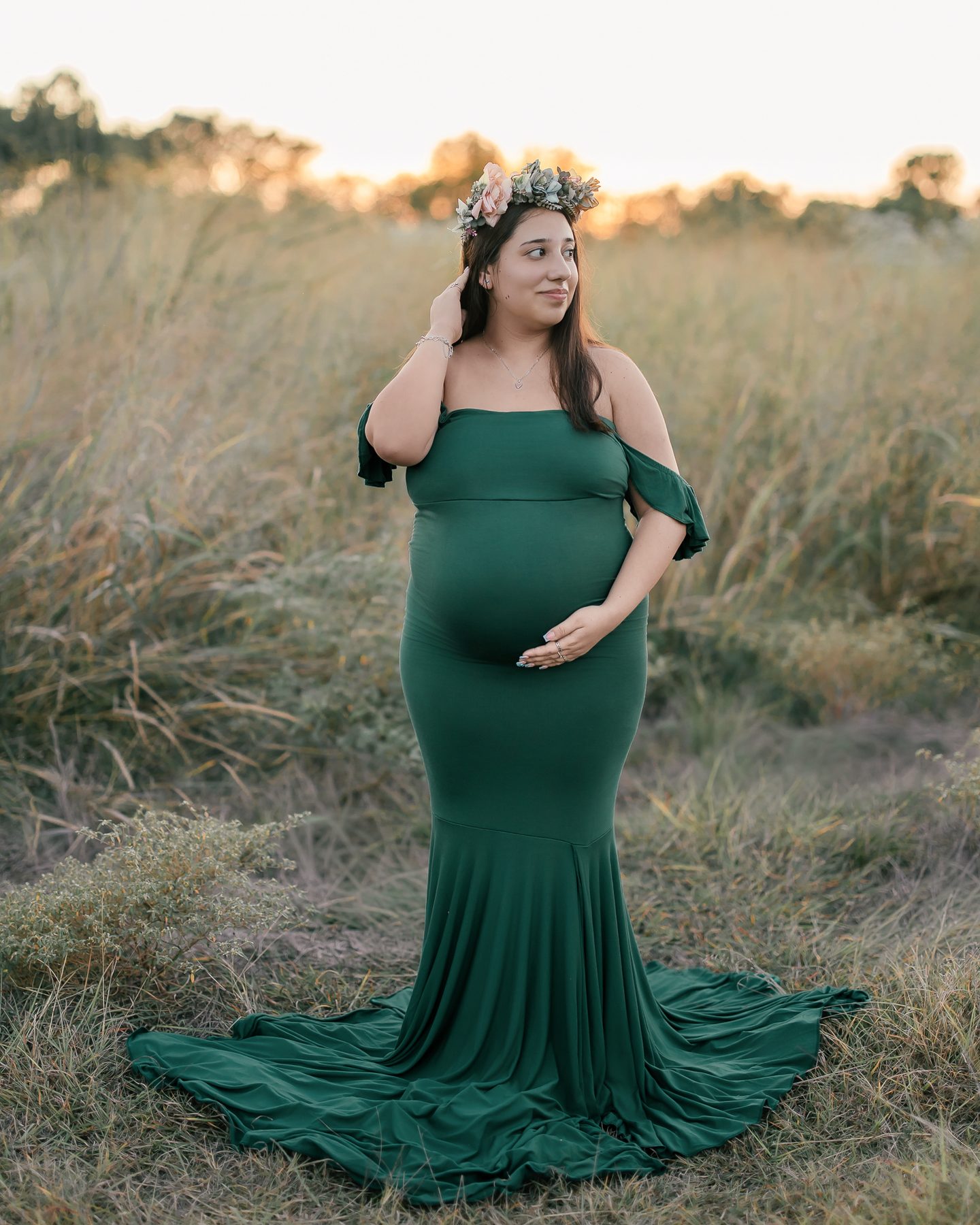 Maternity portrait in a green gown in a field at sunset
