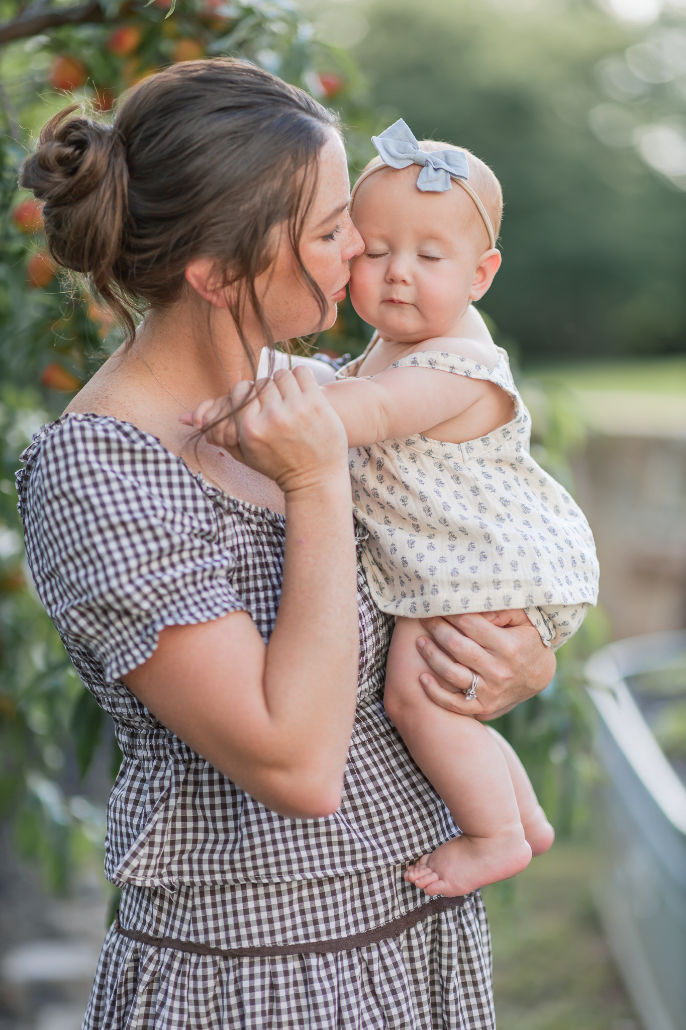 Mom kissing her baby girl's cheek beside a peach tree