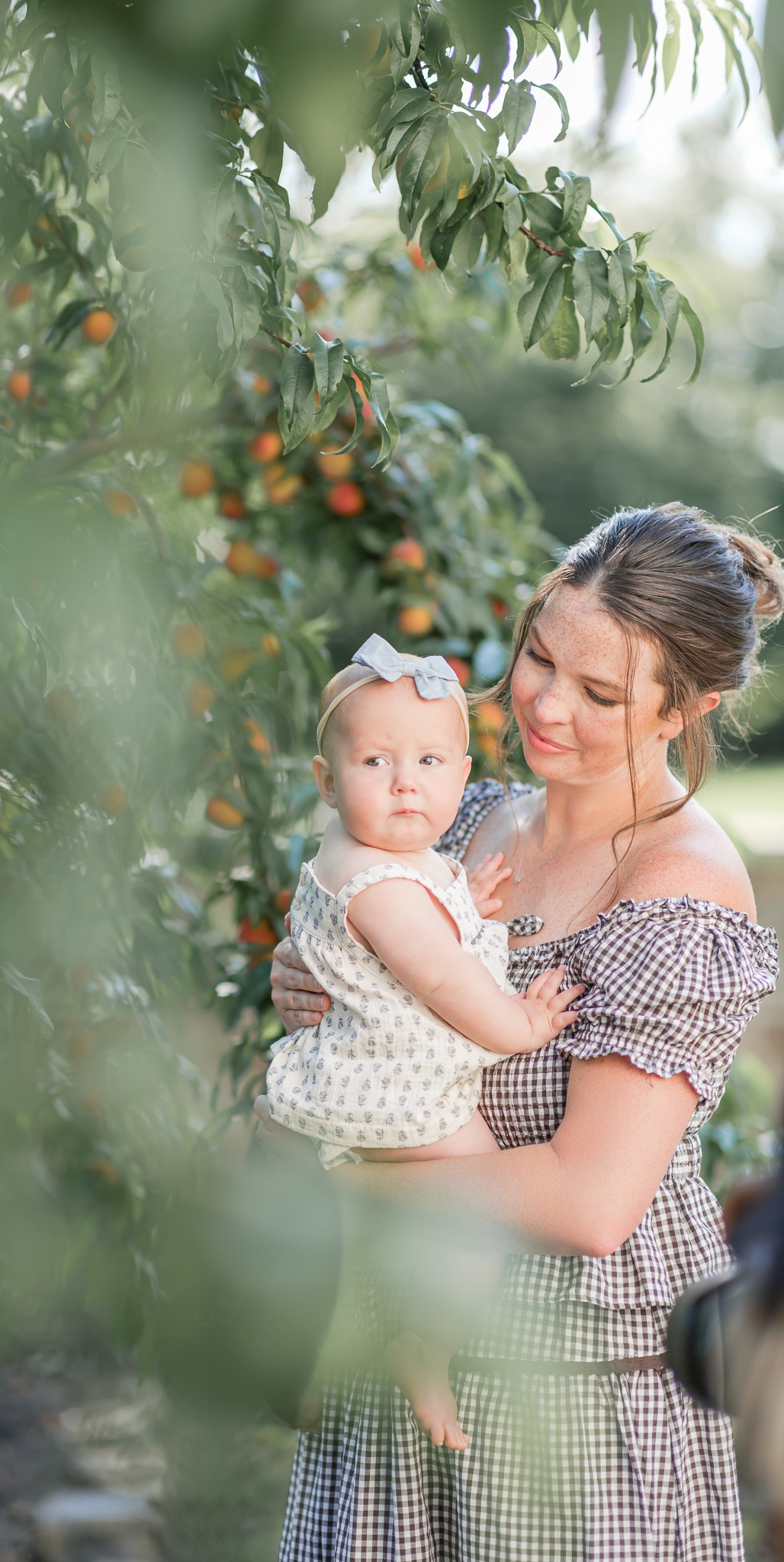 Mom holding her baby girl, framed by peach tree leaves