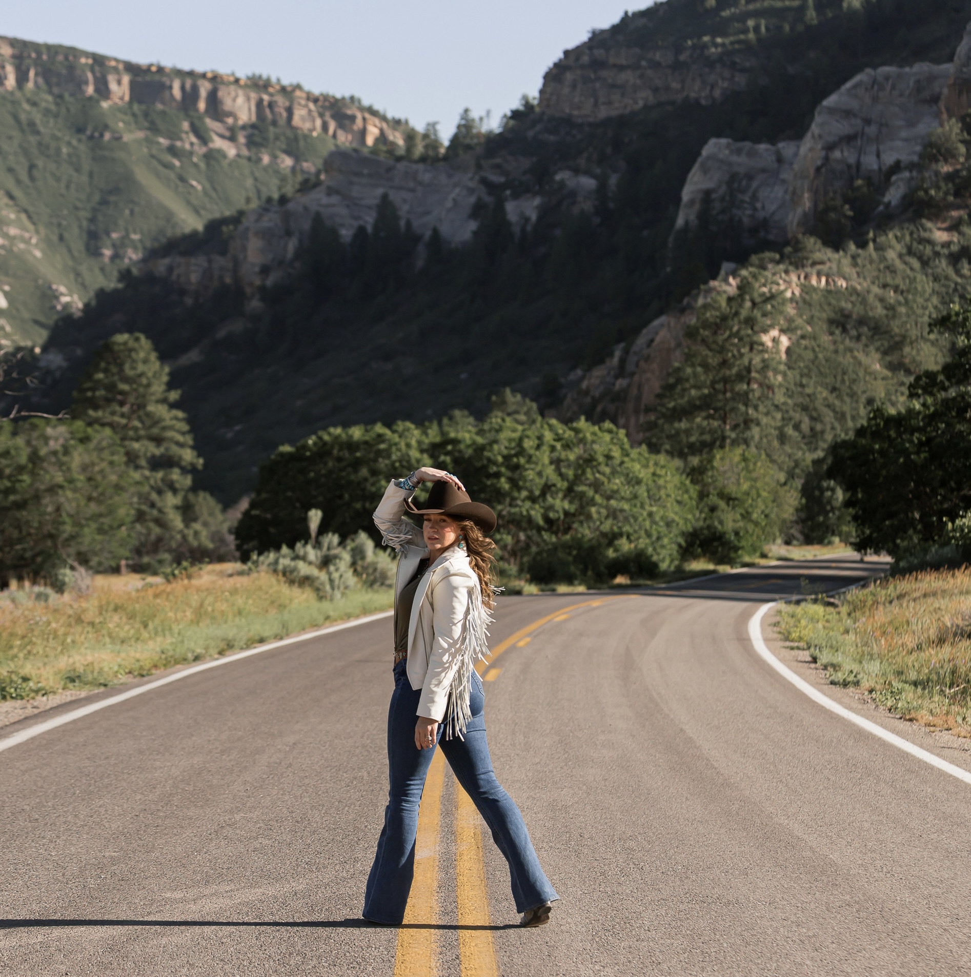 Western portrait of a woman in a fringe jacket on a winding canyon road