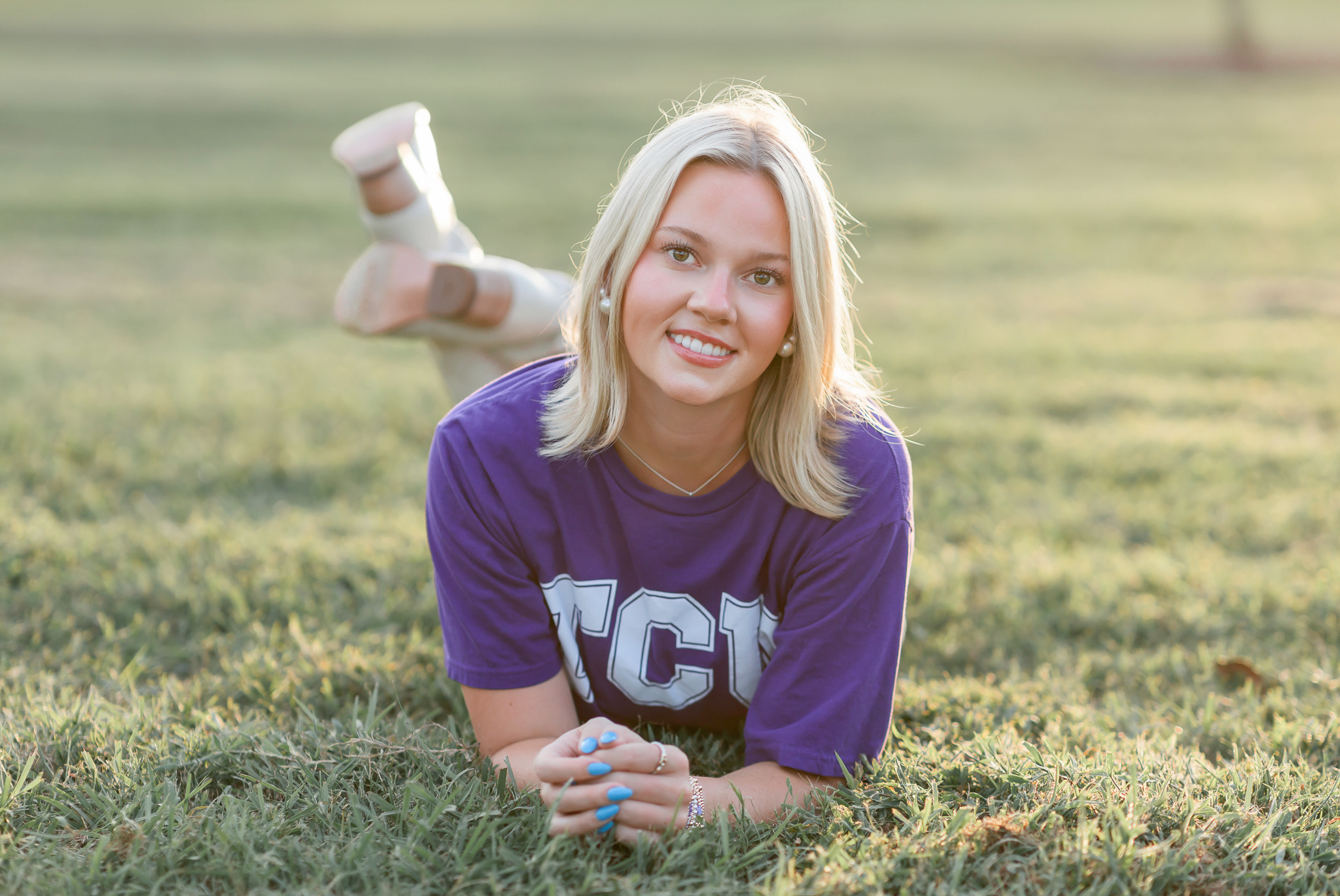 Senior in a TCU shirt lying in the grass, smiling